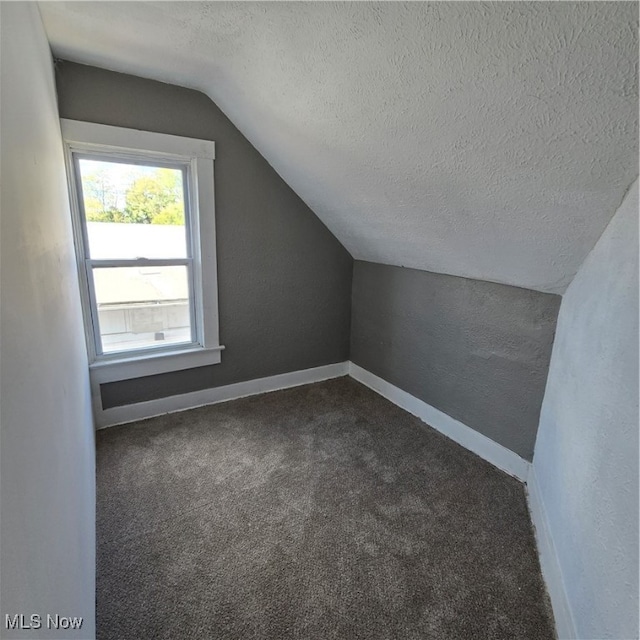 bonus room featuring dark colored carpet, a textured ceiling, and vaulted ceiling