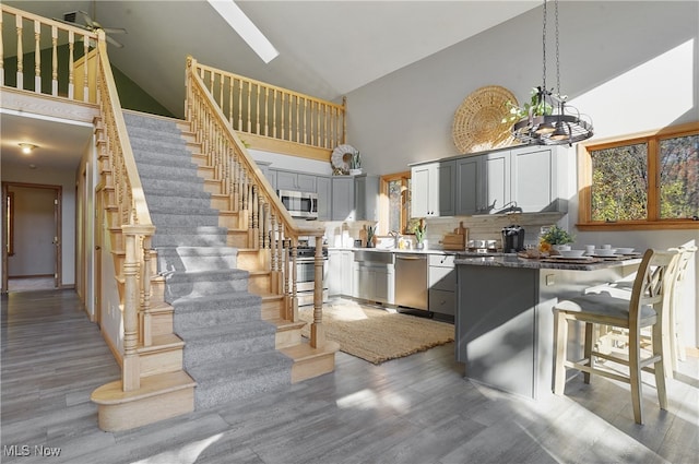 kitchen with gray cabinetry, hardwood / wood-style floors, stainless steel appliances, decorative light fixtures, and high vaulted ceiling