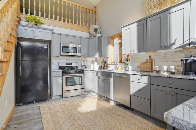 kitchen with gray cabinetry, stainless steel appliances, light stone countertops, high vaulted ceiling, and tasteful backsplash