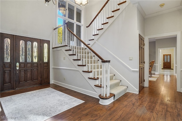 entryway with ornamental molding, a chandelier, dark hardwood / wood-style floors, and a towering ceiling