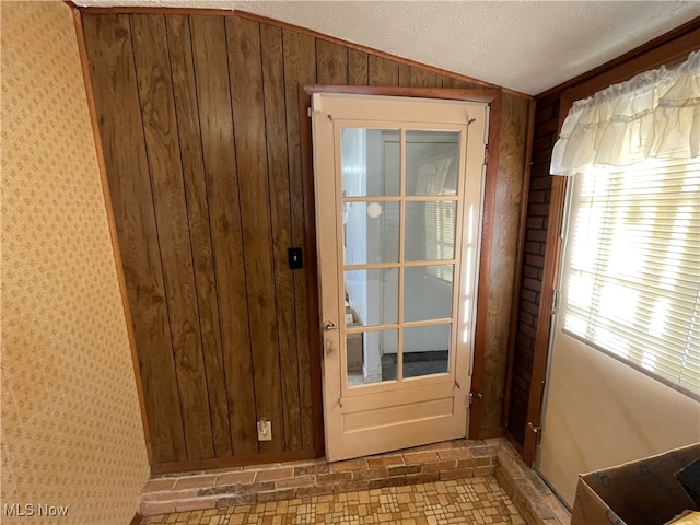 entryway with wood walls, a textured ceiling, and vaulted ceiling