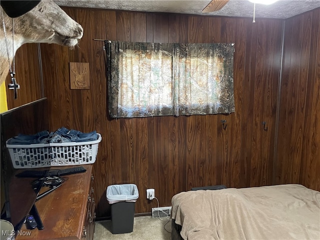 carpeted bedroom with ceiling fan, wood walls, and a textured ceiling