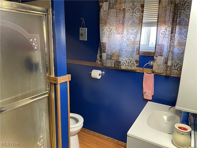 bathroom featuring toilet, hardwood / wood-style flooring, a shower with shower door, and vanity