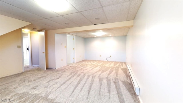 basement with a drop ceiling, light carpet, and a baseboard heating unit