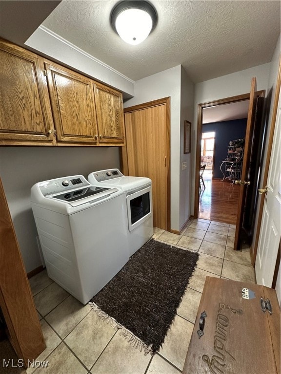 laundry area with independent washer and dryer, a textured ceiling, cabinets, and light tile patterned floors