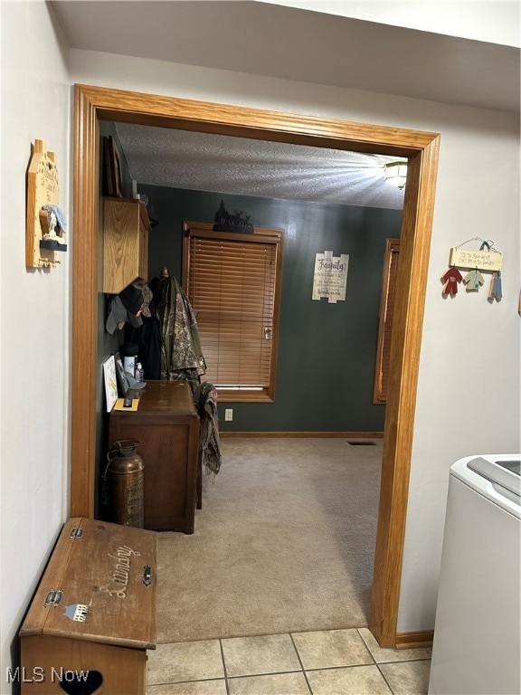 hall featuring light tile patterned flooring, a textured ceiling, and washer / clothes dryer