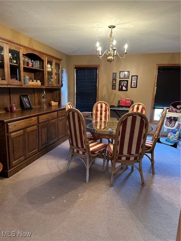 carpeted dining room featuring a notable chandelier and a textured ceiling