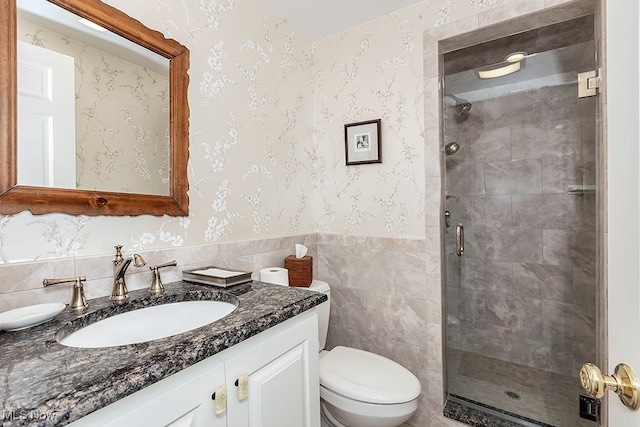 bathroom with a shower with door, vanity, toilet, and tile walls