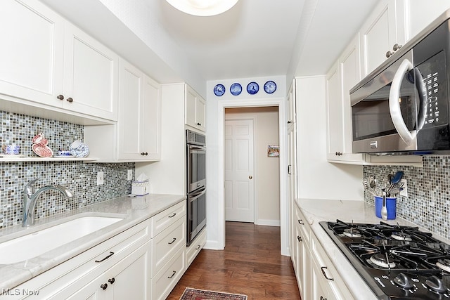 kitchen with light stone countertops, appliances with stainless steel finishes, backsplash, white cabinetry, and dark wood-type flooring