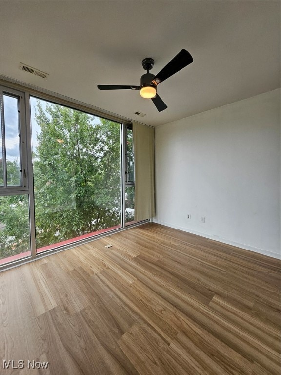 unfurnished room with ceiling fan, wood-type flooring, and a wall of windows