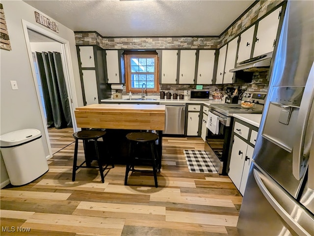 kitchen featuring white cabinetry, light hardwood / wood-style floors, appliances with stainless steel finishes, and a kitchen bar