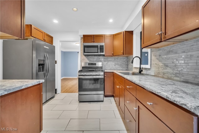 kitchen featuring sink, light hardwood / wood-style flooring, decorative backsplash, light stone counters, and stainless steel appliances