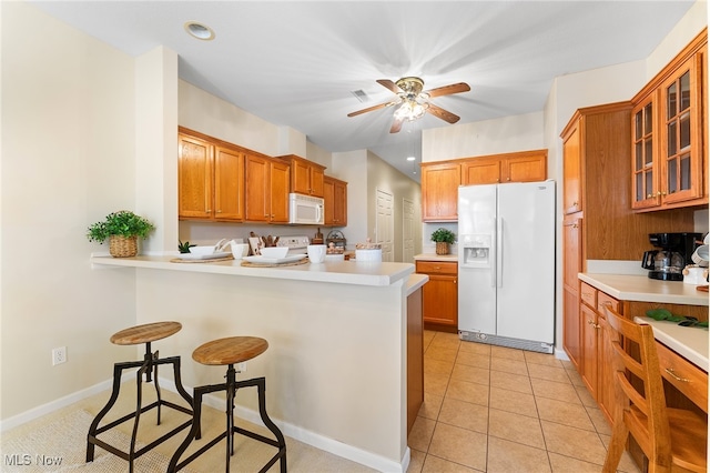 kitchen with a breakfast bar area, kitchen peninsula, light tile patterned flooring, white appliances, and ceiling fan