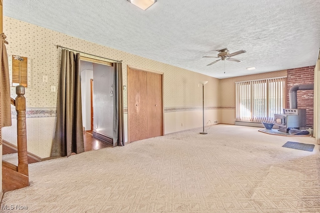 empty room featuring a textured ceiling, carpet floors, a wood stove, and ceiling fan