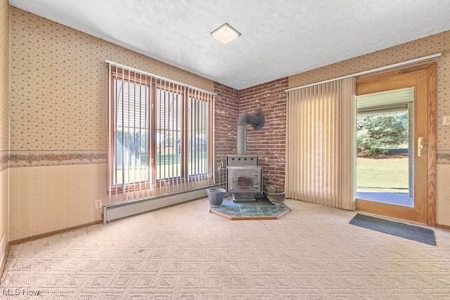 unfurnished living room with baseboard heating, light carpet, a textured ceiling, and a wood stove