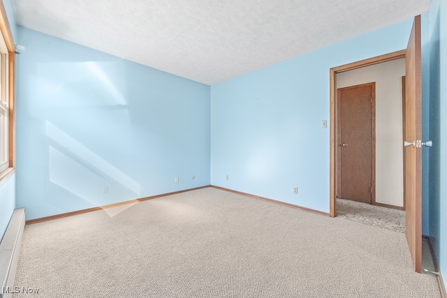 empty room featuring light carpet, a textured ceiling, and baseboard heating