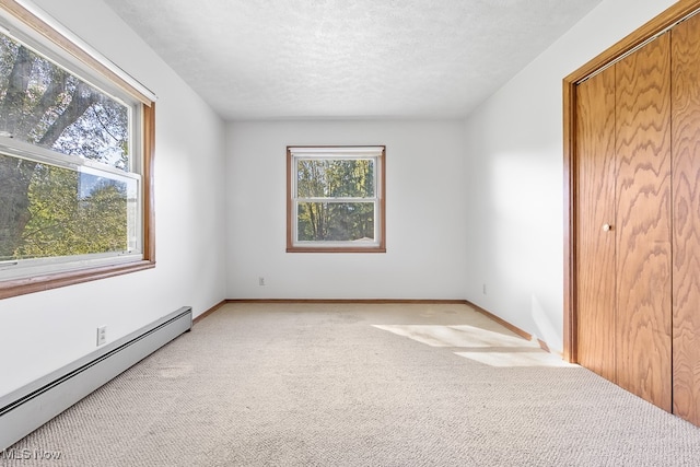 carpeted empty room with baseboard heating, a textured ceiling, and plenty of natural light