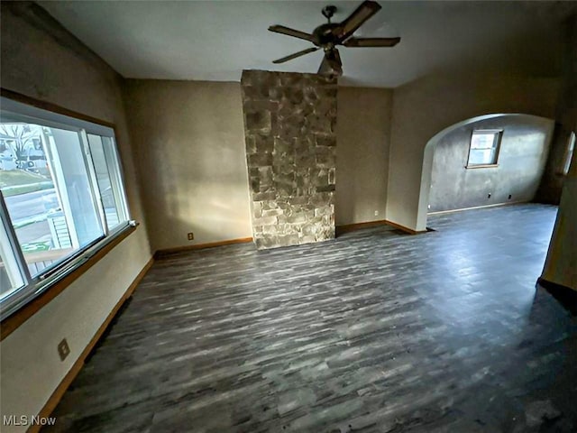 unfurnished living room with arched walkways, ceiling fan, wood finished floors, and baseboards