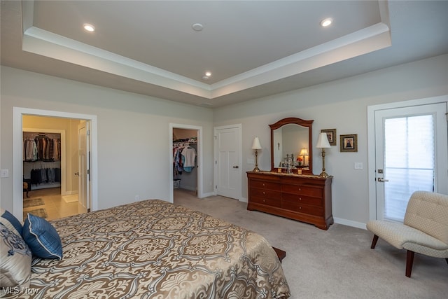 bedroom with a spacious closet, light colored carpet, a closet, and a raised ceiling