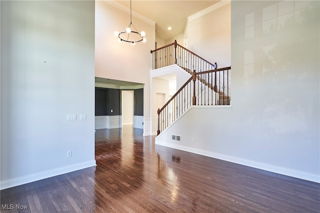 interior space featuring crown molding, a towering ceiling, dark hardwood / wood-style flooring, and a chandelier