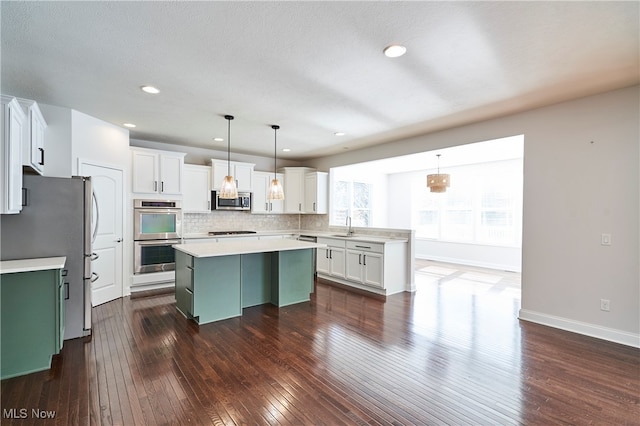 kitchen featuring appliances with stainless steel finishes, a center island, white cabinetry, pendant lighting, and dark hardwood / wood-style floors