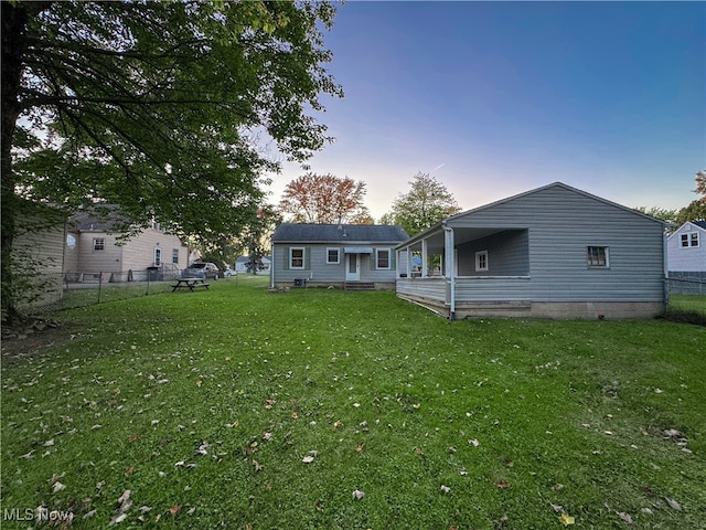 back house at dusk featuring a lawn