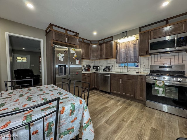 kitchen with decorative backsplash, appliances with stainless steel finishes, light hardwood / wood-style floors, dark brown cabinetry, and sink