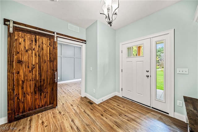 foyer with light wood-type flooring, a barn door, and a notable chandelier