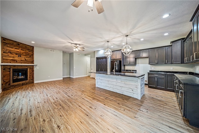 kitchen with a center island with sink, hanging light fixtures, wooden walls, light wood-type flooring, and a large fireplace