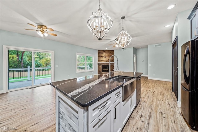 kitchen with sink, light hardwood / wood-style flooring, pendant lighting, fridge, and a center island with sink