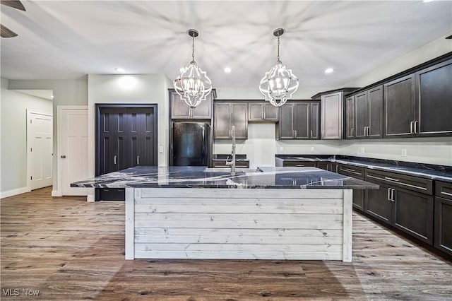 kitchen featuring black refrigerator, decorative light fixtures, a kitchen island with sink, and dark stone counters