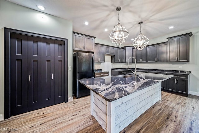 kitchen featuring pendant lighting, black refrigerator, light wood-type flooring, and a kitchen island with sink