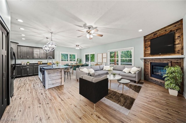 living room with ceiling fan with notable chandelier, a stone fireplace, light wood-type flooring, and a textured ceiling