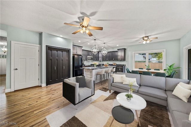 living room with ceiling fan with notable chandelier, light hardwood / wood-style floors, and sink