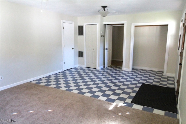 unfurnished bedroom featuring dark colored carpet and two closets