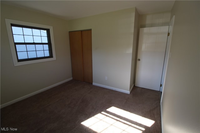 unfurnished bedroom with dark colored carpet and a closet