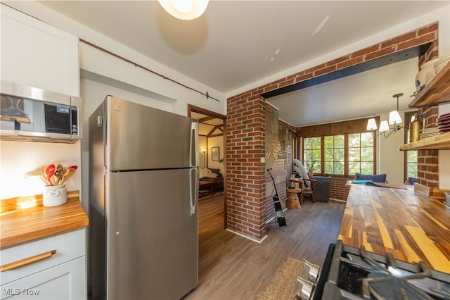 kitchen featuring white cabinetry, butcher block counters, hanging light fixtures, and stainless steel refrigerator