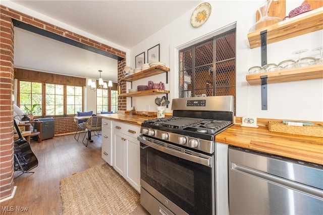 kitchen with wooden counters, appliances with stainless steel finishes, hanging light fixtures, and white cabinetry