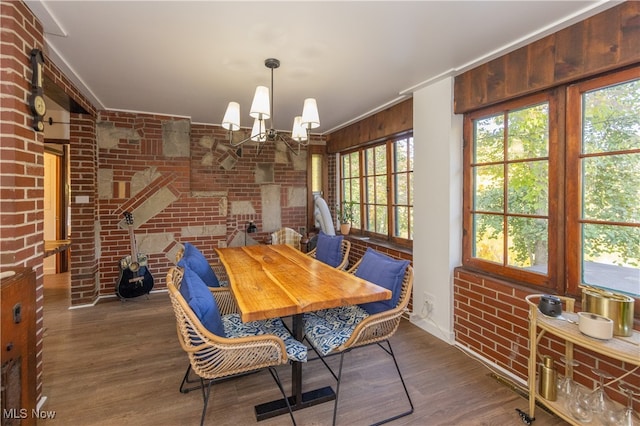 dining area with dark wood-type flooring, brick wall, and an inviting chandelier