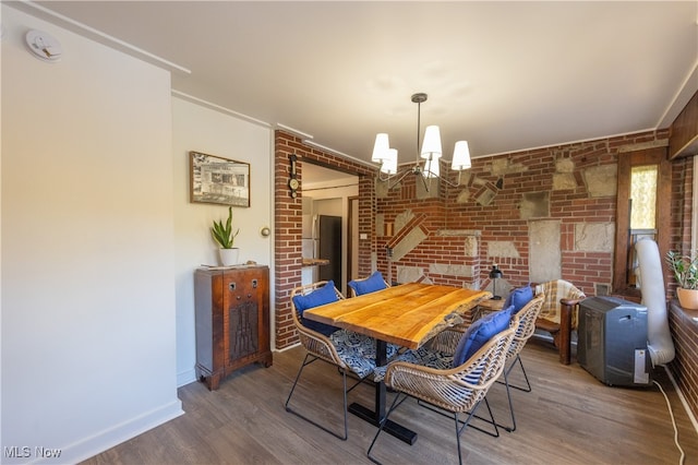 dining room with an inviting chandelier, hardwood / wood-style flooring, and brick wall