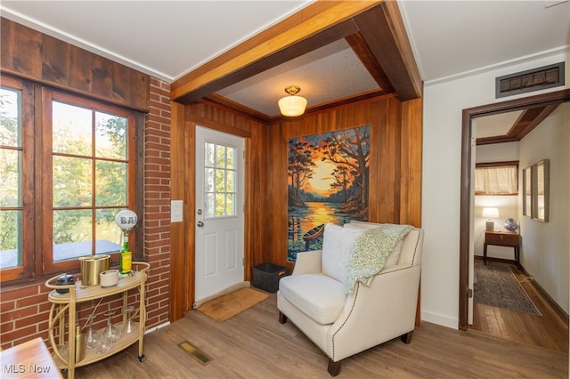 living area with ornamental molding, beam ceiling, wooden walls, and wood-type flooring