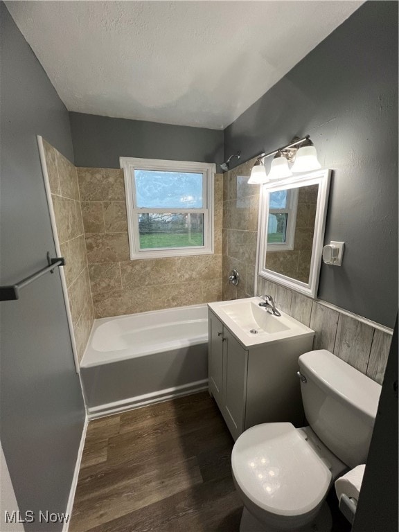 full bathroom featuring wood-type flooring, a textured ceiling, toilet, tiled shower / bath, and vanity