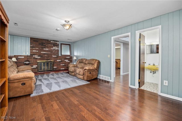 living room with wooden walls, a brick fireplace, and dark hardwood / wood-style floors