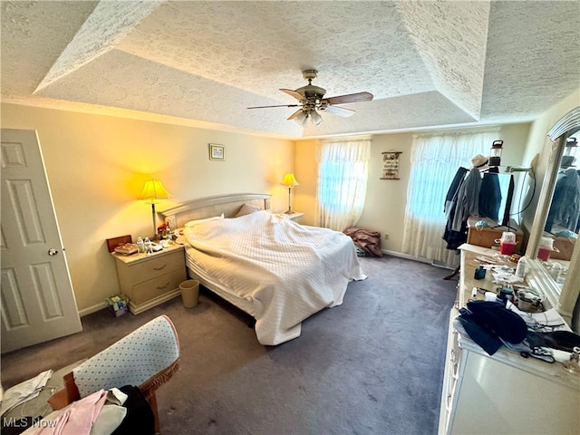 bedroom with dark colored carpet, ceiling fan, and a raised ceiling