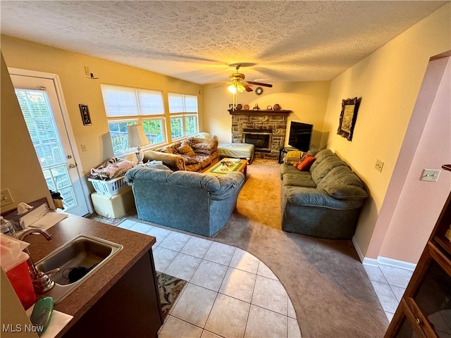 tiled living room with sink, a stone fireplace, a textured ceiling, and ceiling fan