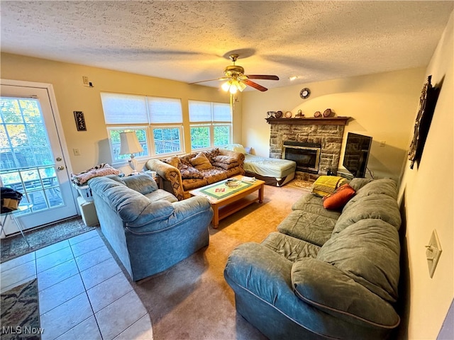 tiled living room with ceiling fan, a stone fireplace, and a textured ceiling