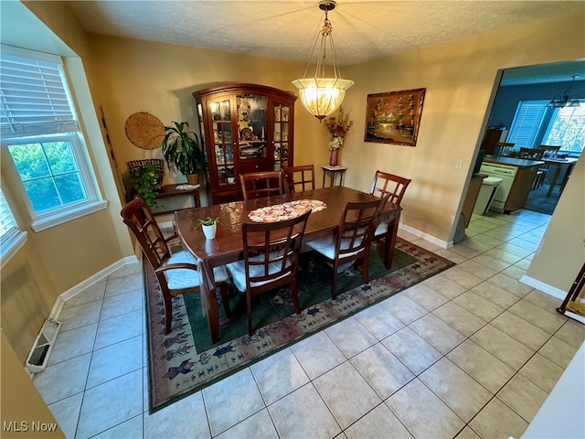 dining room with a healthy amount of sunlight, a textured ceiling, light tile patterned floors, and an inviting chandelier