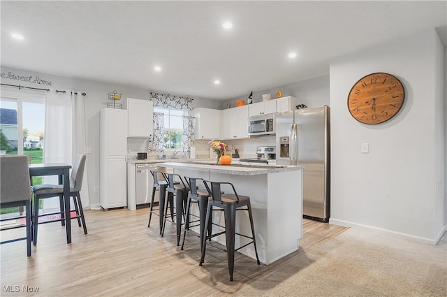 kitchen with white cabinets, a kitchen breakfast bar, light wood-type flooring, stainless steel appliances, and a center island