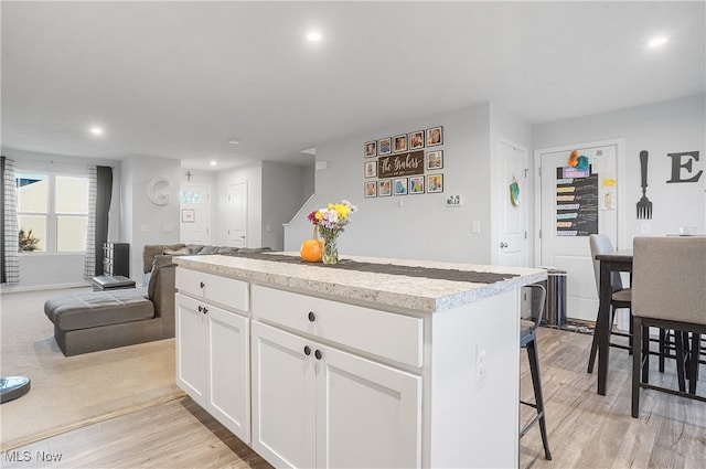 kitchen with white cabinetry, light wood-type flooring, a kitchen island, and a kitchen breakfast bar