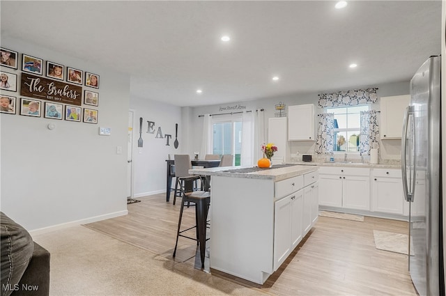 kitchen with a center island, light hardwood / wood-style flooring, white cabinets, and stainless steel refrigerator